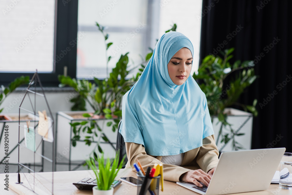 young muslim woman typing on laptop in office on blurred foreground young muslim woman typing on laptop in office on blurred foreground