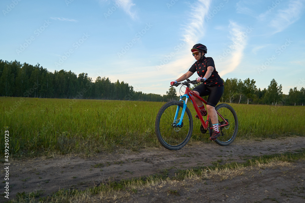 The girl rides a mountain bike on a country road. Outdoor endurance training. Dressed in a bicycle uniform and a helmet. Side view. Healthy lifestyle.