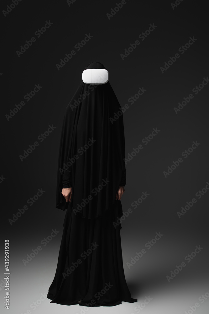 full length view of muslim nun in black abaya and vr headset on black background full length view of muslim nun in black abaya and vr headset on black background