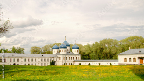  Yellow dandelions grow in the clearing in front of the blue-domed temple. The sun illuminates the white clouds. © ALLA