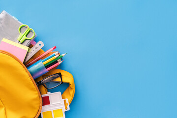 School supplies sticking out of a backpack on a blue background. Back to school concept