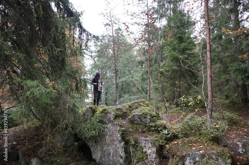 a girl stands with her back on a large stone in the park