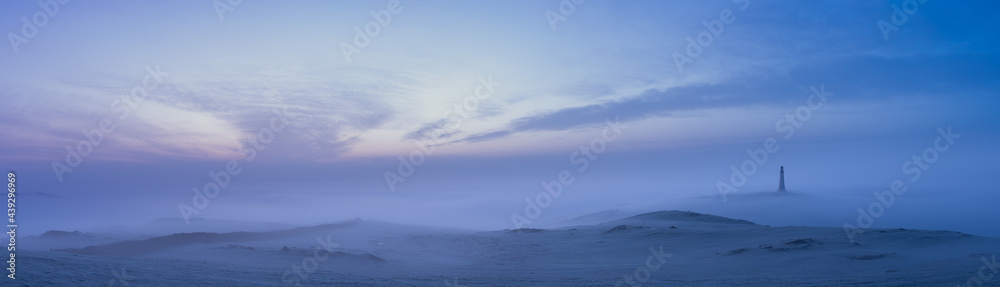 A lighthouse at dawn in the mist and fog under a purple sky