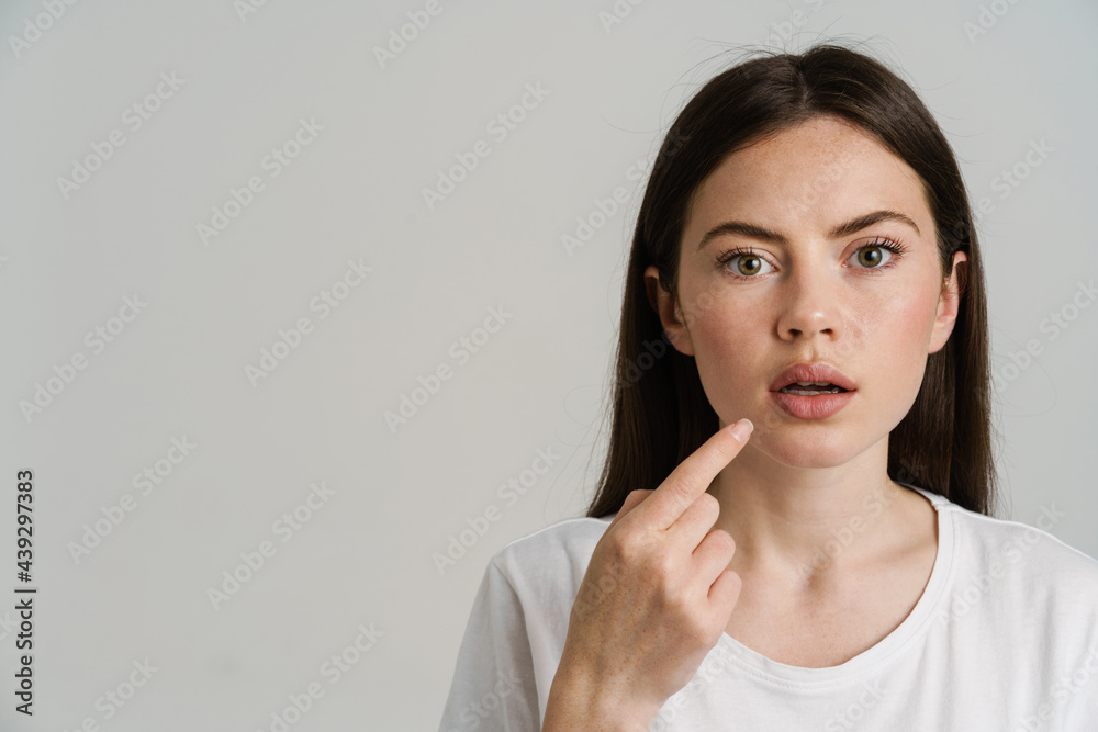 Surprised woman pointing finger at her mouth and looking at camera Surprised woman pointing finger at her mouth and looking at camera