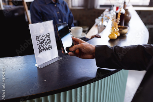 Mid section of man making a payment by scanning qr code from smartphone at a cafe