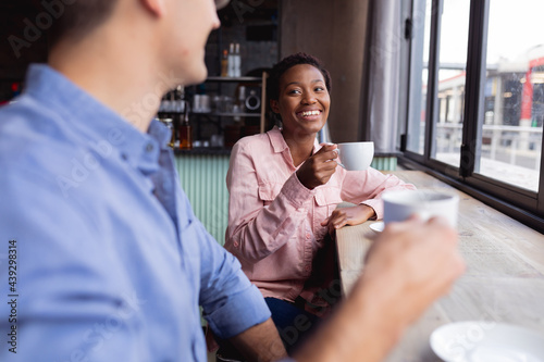 Mixed race couple holding coffee cups smiling while sitting at a cafe photo