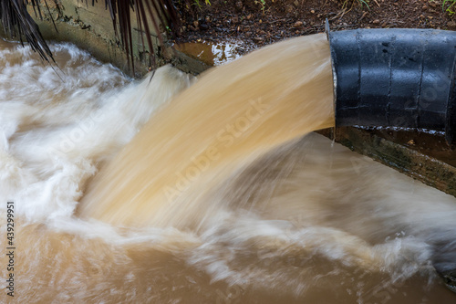 A close-up view of water violently flowing from a steel pipe near the concrete shore.