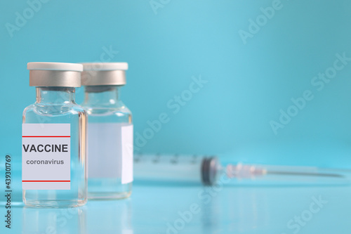 Glass vials containing liquid medical vaccine used to shot for injection treatment with blurred needle syringe on blue background and copy space, vaccination and immunization care for preventing coron