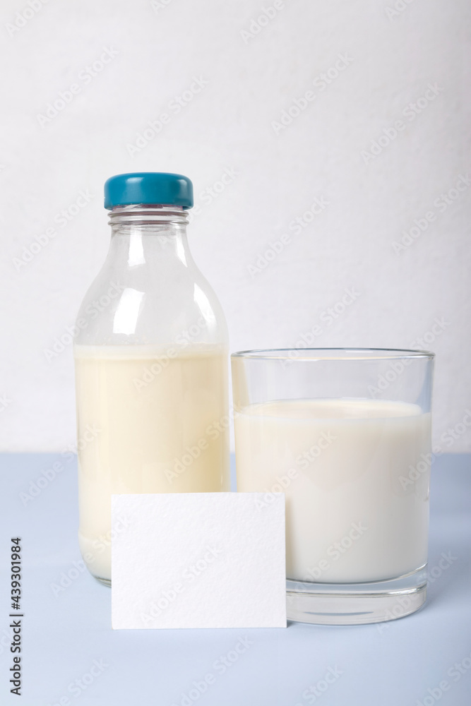 Bootle and glass of milk, white card for information about milk on the blue surface agaist white wall Bootle and glass of milk, white card for information about milk on the blue surface agaist white wall