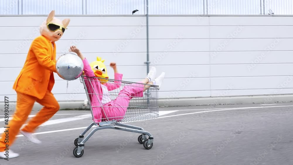 Pig man pushing bird woman with disco ball in shopping cart