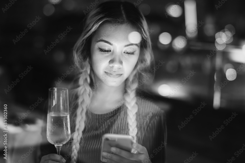 Serious young woman using a smartphone at a rooftop bar in the e Serious young woman using a smartphone at a rooftop bar in the e