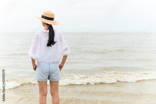 Outdoor summer portrait of young asian woman in straw hat looking to the sea at tropical beach, enjoy freedom time, fresh air and leisure travel vacation.