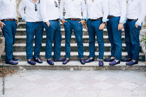 Seven groom's best men in identical blue trousers and shoes stand on the stairs, close-up 
