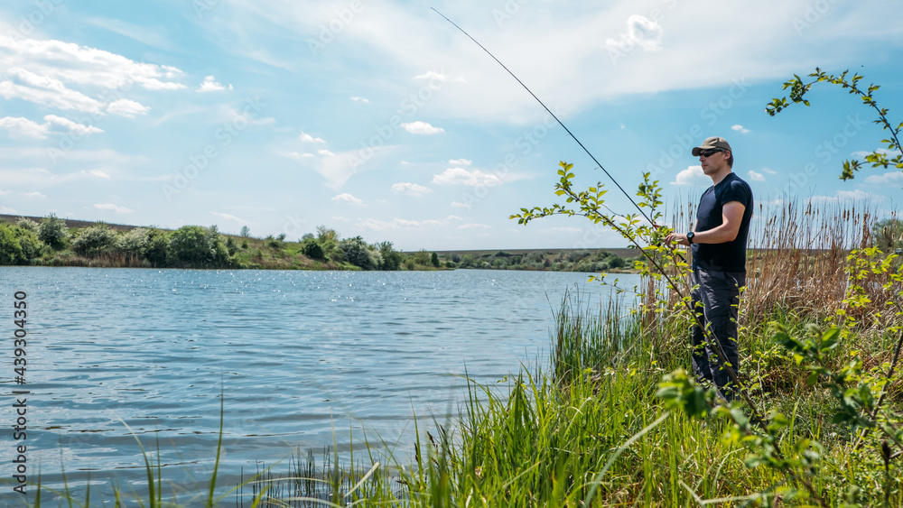 Fisherman with spinning rod on nature background. Angler man with fishing spinning or casting rod by the river. Fisherman with rod, spinning reel on the river bank Fisherman with spinning rod on nature background. Angler man with fishing spinning or casting rod by the river. Fisherman with rod, spinning reel on the river bank