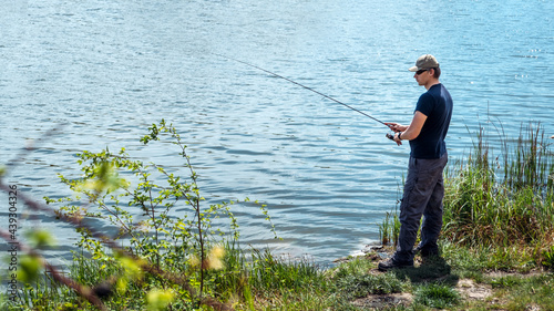 Fisherman with spinning rod on nature background. Angler man with fishing spinning or casting rod by the river. Fisherman with rod, spinning reel on the river bank