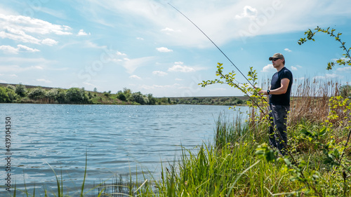 Fisherman with spinning rod on nature background. Angler man with fishing spinning or casting rod by the river. Fisherman with rod, spinning reel on the river bank
