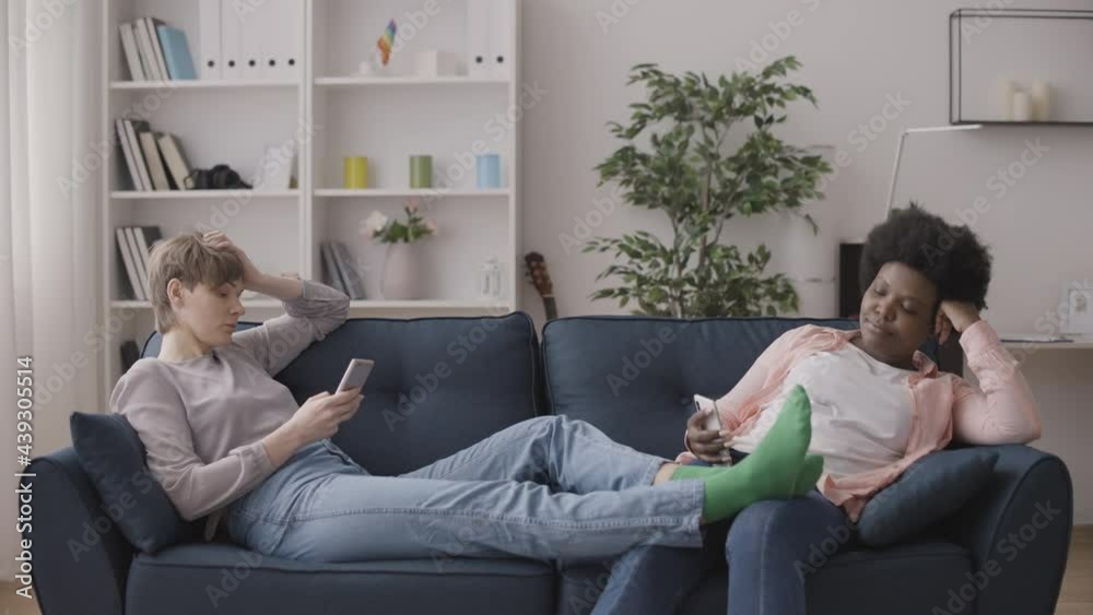 Two women addicted to gadgets sitting on couch, scrolling smartphones silently Two women addicted to gadgets sitting on couch, scrolling smartphones silently