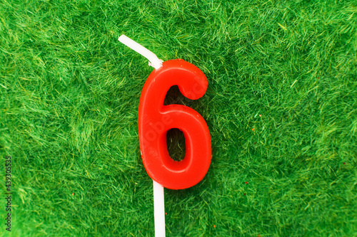 candle in the form of number 6 on the green grass background, a place for a greeting text photo