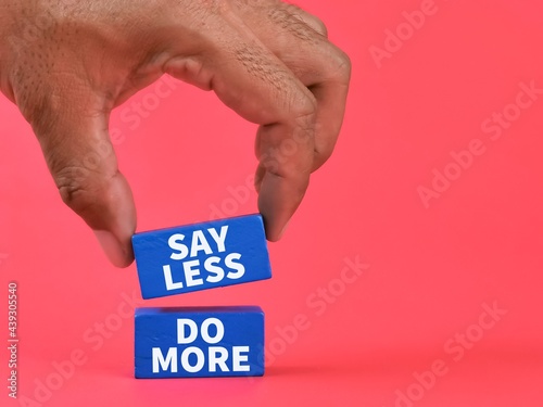 Phrase say less do more on blue wooden blocks against red background.