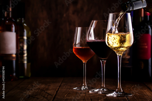 Wine tasting. Whte wine pouring into glass on background with selection of red, white and rose wines in glasses and bottles