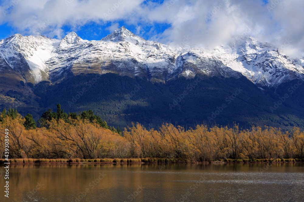 A lake surrounded by autumn willow trees, with snowy mountains behind. Photographed at the Glenorchy Lagoon, New Zealand, looking towards the Southern Alps