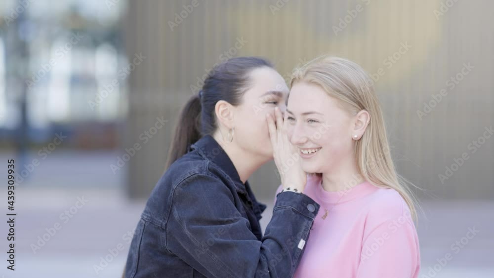 Young woman whispering secret in friends ear Young woman whispering secret in friends ear