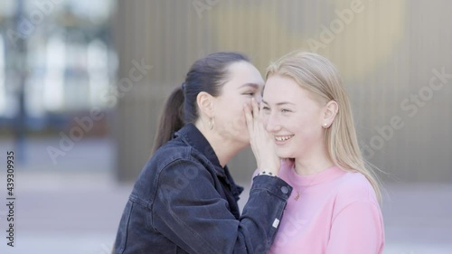 Young woman whispering secret in friends ear