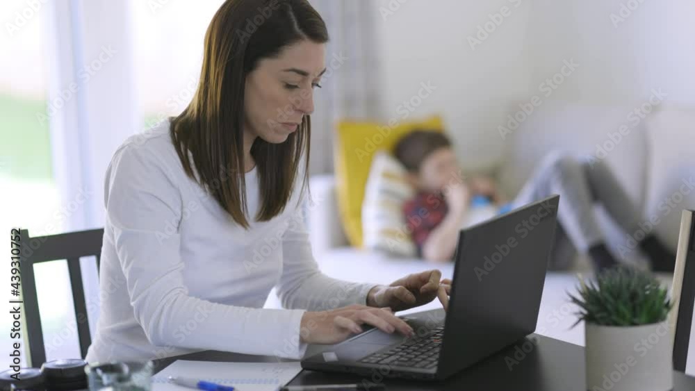 Working mother typing on laptop with son in background