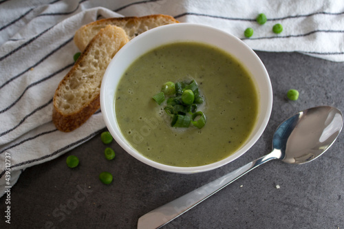 Green peas soup in a white bowl, fresh baguette bread on striped kitchen towel. Vegetarian meal top view photo. Eating fresh concept. 