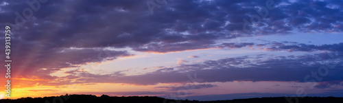 Panorama of a beautiful sunset with purple clouds and sunbeams to the horizon