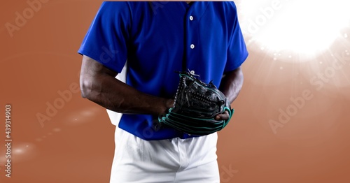 Mid section of african american male baseball pitcher against spot of light on orange background