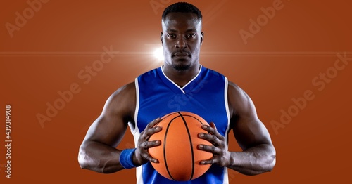 African american male basketball player holding basketball against spot of light in background
