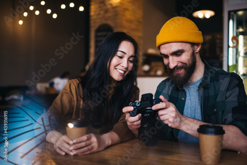 Smiling couple watching photos in camera while sitting in cafe with cups of coffee