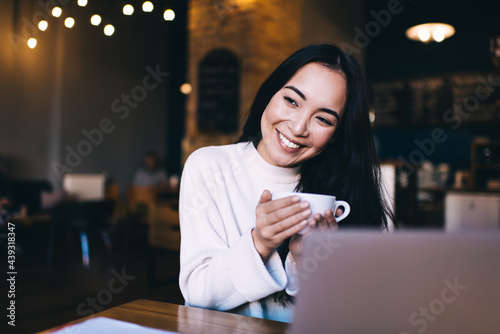 Happy woman with cup of hot drink smiling in cafe
