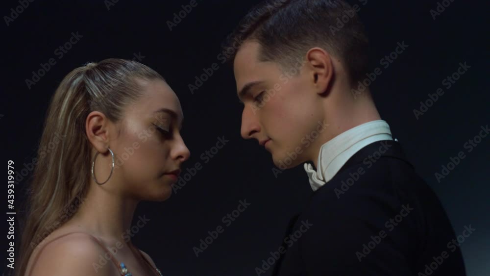 Ballroom couple standing in dark background. Young dancers looking each other.