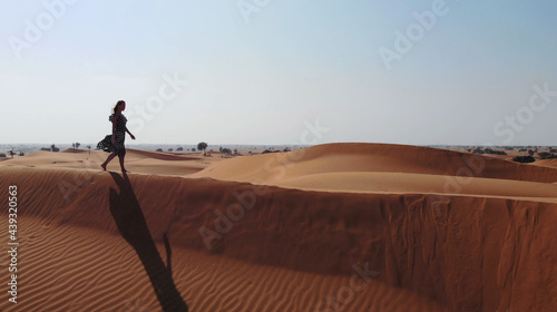 AERIAL. Woman weared in long dress walking in the Dubai desert sand dunes with footsteps in the sand during sunset