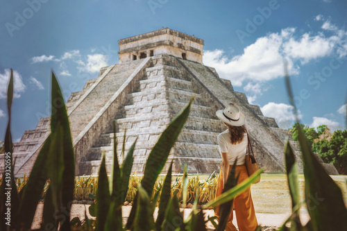 A young woman tourist in a hat stands against the background of the pyramid of Kukulcan in the ancient Mexican city of Chichen Itza. Travel concept.Mayan pyramids in Yucatan, Mexico photo