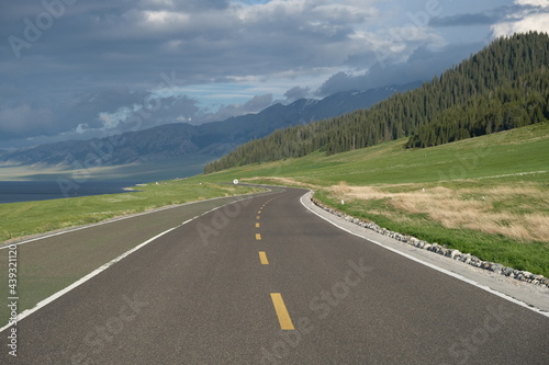 empty winding asphalt road at grassland. Forest and mountain range background