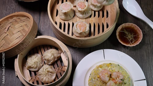 Prawn shrimp shaomai pickup by chopsticks Xiao long bao dim sum dumpling chicken prawn fish seafood vegetable in bamboo steamer fried rice on plate sauce soup spoon over rustic background photo