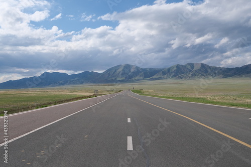 empty straight asphalt road at grassland. Mountain and white clouds background