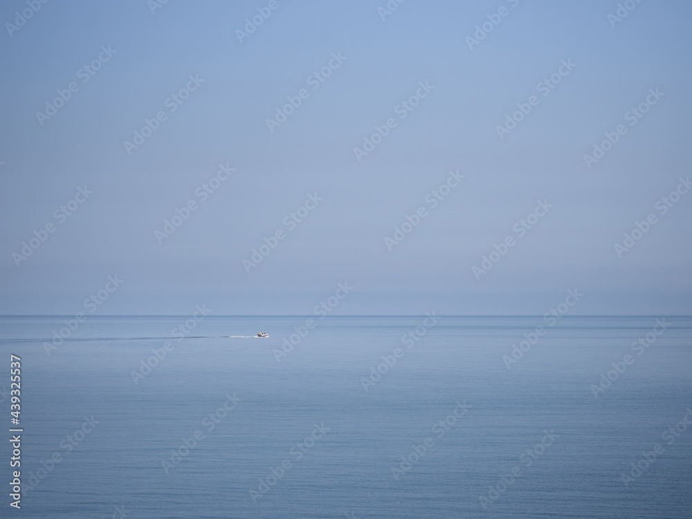 Big sea, small boat. Plain blue sky and horizon.