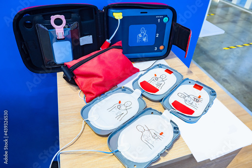 Automatic external defibrillator. Portable defibrillator on a wooden table. Defibrillator for medical care. Device for provision of emergency medical care. Automatic cardioverter with nursing manual photo