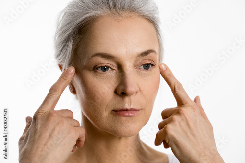 Woman touching her skin near the eyes and showing her little mimic wrinkles photo