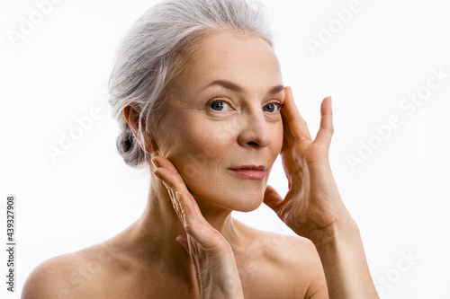 Woman with grey hair pulls the skin with her hands while demonstrating face lifting photo