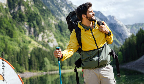 Hiker young man with backpack and trekking poles looking at the mountains in outdoor photo