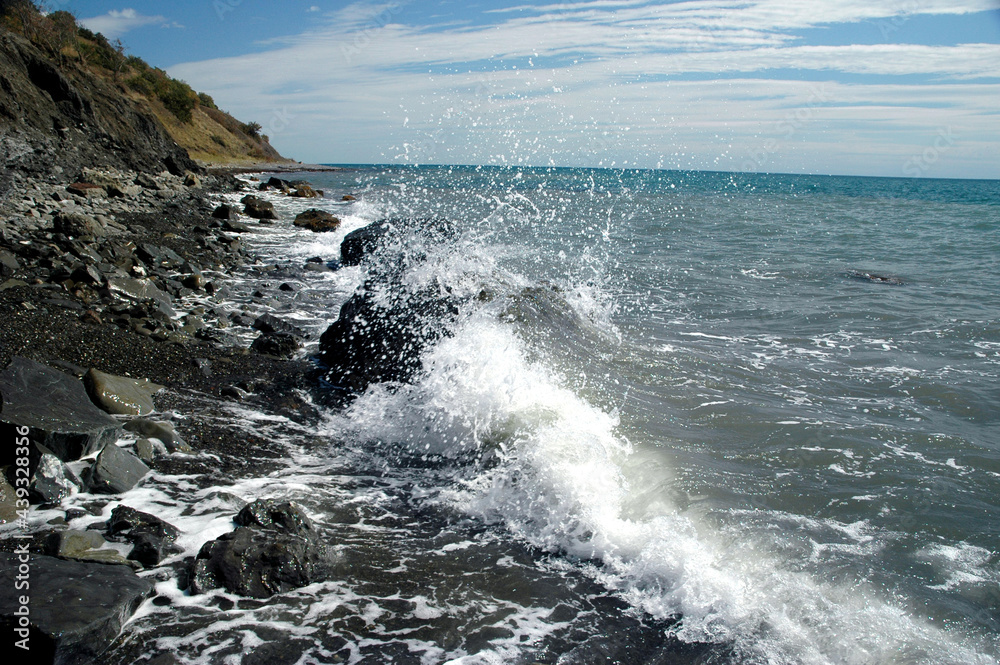 A rocky beach, the stones are washed by foamy waves. Mountains are visible on the horizon.