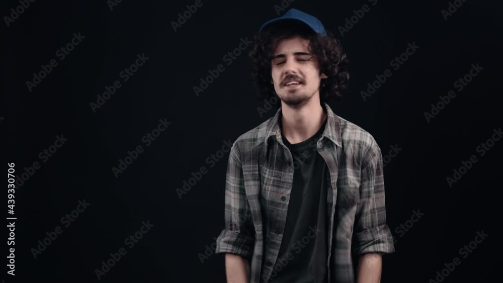 The charismatic and happy hipster boy looks to one side, with a cap on his head, says wow and shows the like sign. Isolated on black background. The concept of life. People's emotions. 4k portrait The charismatic and happy hipster boy looks to one side, with a cap on his head, says wow and shows the like sign. Isolated on black background. The concept of life. People's emotions. 4k portrait