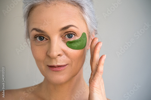 Woman applying anti-fatigue under-eye mask while looking at the camera photo