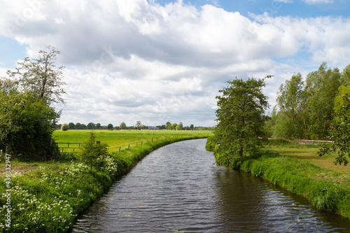 The river, called De Barneveldse beek, flows gently through the flat farm landscape.