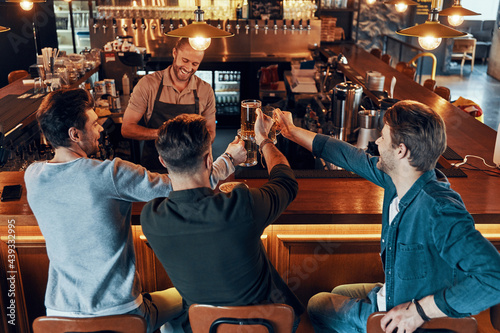 Top view of carefree young men in casual clothing drinking beer while sitting in the pub